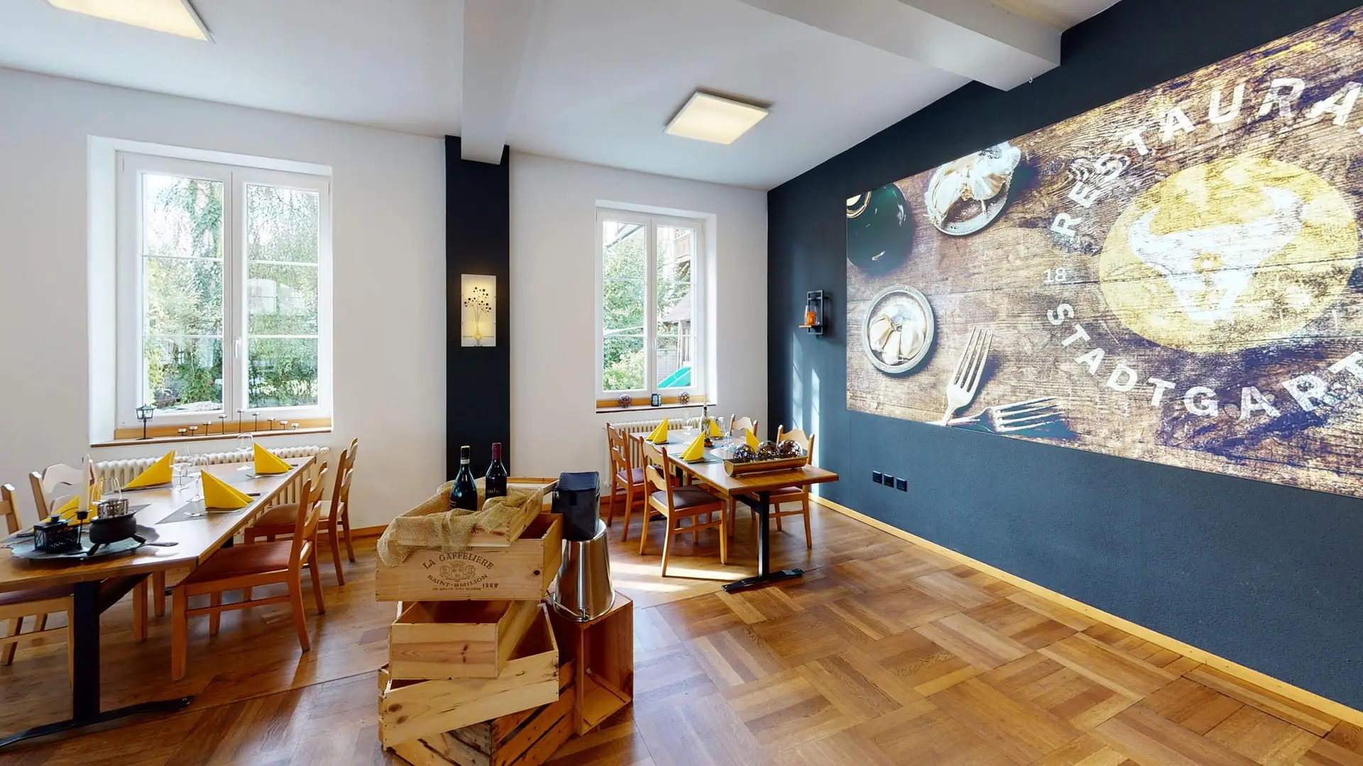 Speisesaal des Restaurant Stadtgarten Wangen mit Wandmural und gedeckten Tischen mit Weinkisten