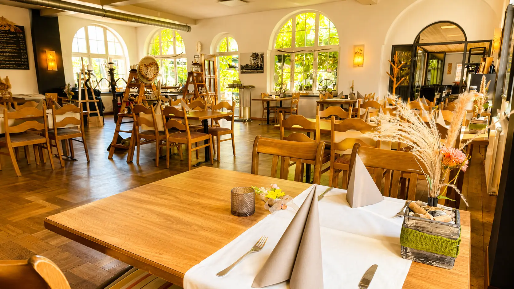 Gedeckter Tisch mit Blumen und Kerzen vor den Bogenfenstern im Speisesaal des Restaurant Stadtgarten Wangen