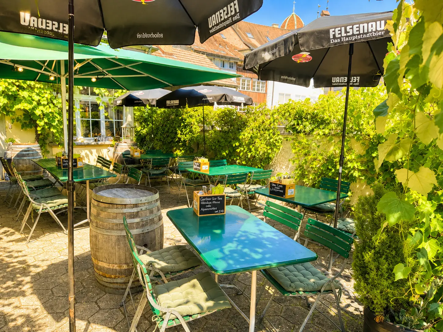 Sonnige Gartenterrasse mit Sonnenschirmen und Gartenmöbeln im Restaurant Stadtgarten Wangen
