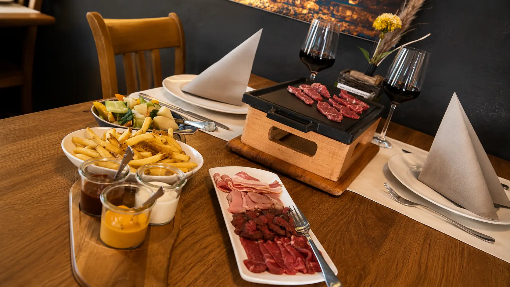 Gedeckter Tisch mit TischGrill, Platte mit rohem Rind, Pferd und Speck, dazu Saucen, Bärner Frites und Gemüse im Restaurant Stadtgarten Wangen an der Aare